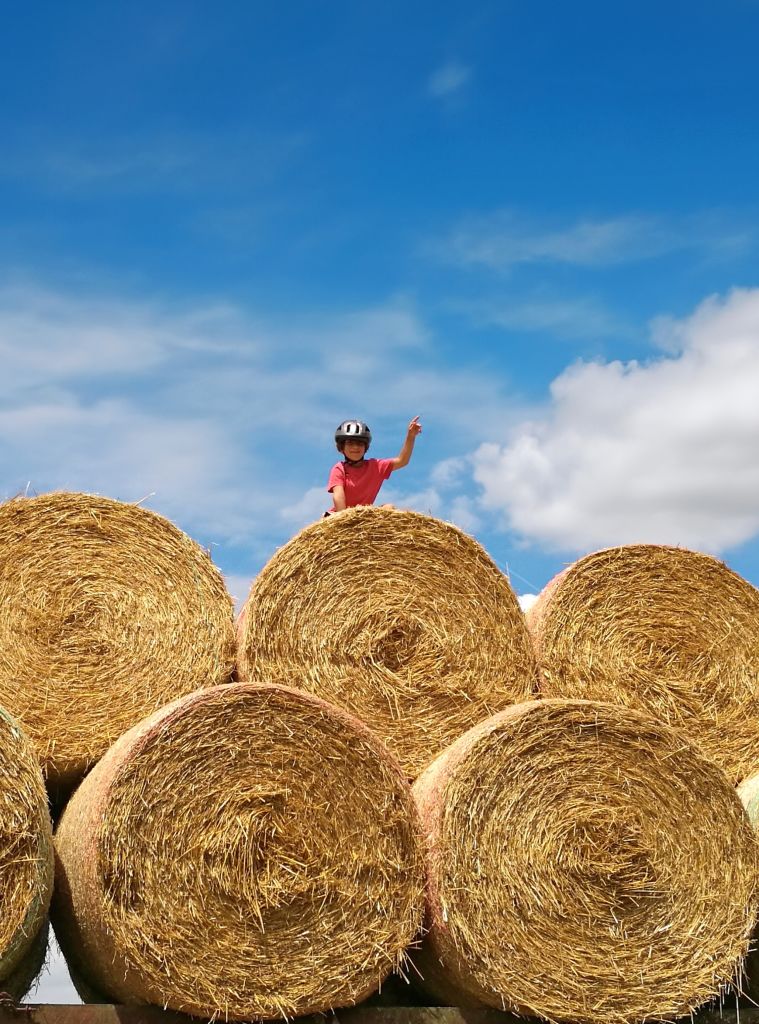 Bambino seduto su grandi balle di fieno sotto il cielo azzurro. Tour in bicicletta per famiglie Francia